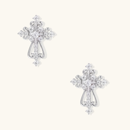 White gold-plated baroque cross studs with zirconia stones and ornate scrollwork on cream background.