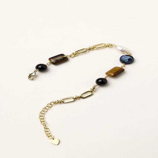 Gold chain bracelet with tiger's eye, obsidian, pearl, and iridescent abalone stones on cream background.