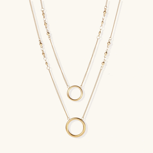 Layered gold necklace set with two open circle pendants and mixed chain styles on beige background