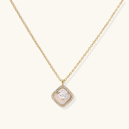 Gold quatrefoil pendant with crystal center on iridescent mother-of-pearl base, adjustable gold chain on cream background