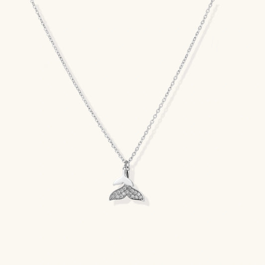 Delicate white gold plated whale tail pendant with pavé crystals on silver chain against cream background.