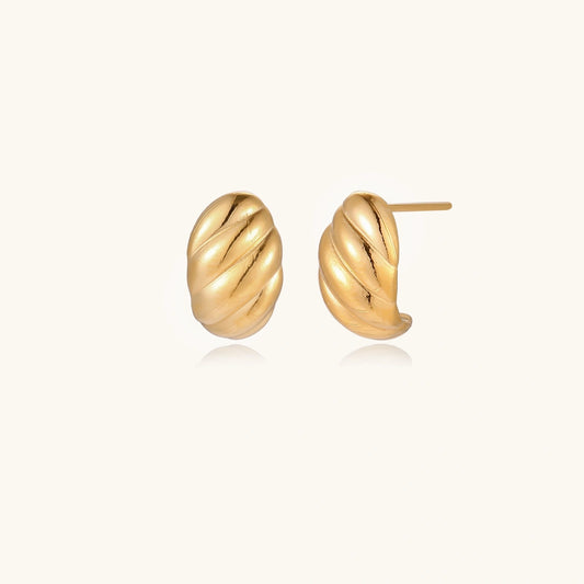 Chunky gold twisted rope huggie hoops with diagonal grooves and high-polish finish on cream background