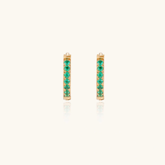 Pair of small gold huggie hoop earrings with bright green cubic zirconia stones on cream background