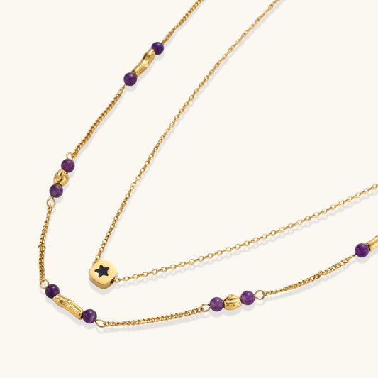 Two layered gold-tone necklaces with purple stone beads and star pendant against cream background.