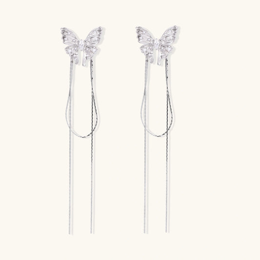 Pair of silver threader earrings with crystal butterfly tops and long chain drops on cream background.
