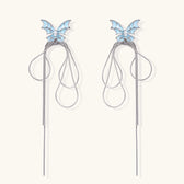 Long silver-tone earrings with powder blue enamel butterfly studs and flowing chain tassels on cream background