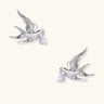 Silver-toned swallow stud earrings with detailed wings carrying teardrop zirconia crystals on white background