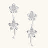 Silver-white asymmetric earrings with textured flower petals and crystal centers on cream background