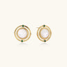 Circular gold stud earrings with iridescent mother-of-pearl center and green zirconia accents on cream background.