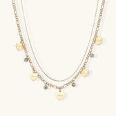 Gold layered necklace set with engraved heart pendants and crystal accents on cream background