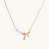Delicate gold necklace with three white pearls and crystal-embellished bow pendant on cream background