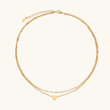 Delicate double-chain gold necklace with tiny heart pendant on cream background