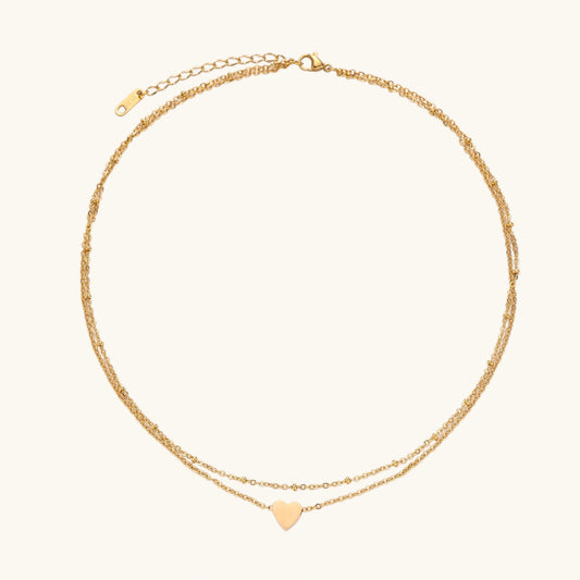 Delicate double-chain gold necklace with tiny heart pendant on cream background