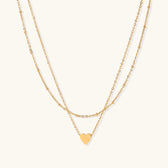 Delicate double-chain gold necklace with tiny heart pendant on cream background