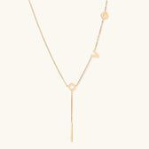 Gold Y-shaped necklace with L-O-V-E letter charms and vertical bar pendant on delicate chain against cream background
