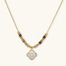Gold-toned beaded necklace with grey stones and quatrefoil abalone shell pendant on cream background.