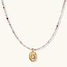 Delicate gold-plated necklace with mixed gemstone beads and ornate oval pendant on white background