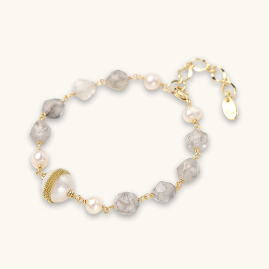 Bracelet with cloudy quartz beads, freshwater pearls, and gold-wrapped baroque pearl centerpiece on white background.
