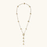 Gold-plated lariat necklace with baroque pearls and textured caps on cream background, showing adjustable Y-shaped design.