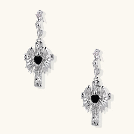 Silver drop earrings with twisted hoops and angel wings embracing black heart locket on white background.